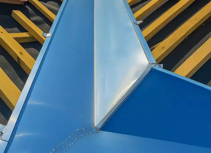 Chantier de construction extérieur avec toiture métallique bleue en cours d'installation sur charpente bois