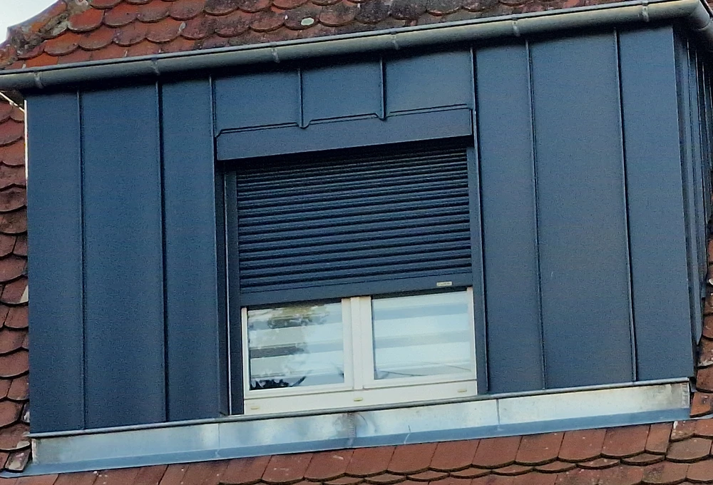 Toiture plate moderne avec lucarne rectangulaire vitrée à cadre noir, installée sur membrane d'étanchéité grise