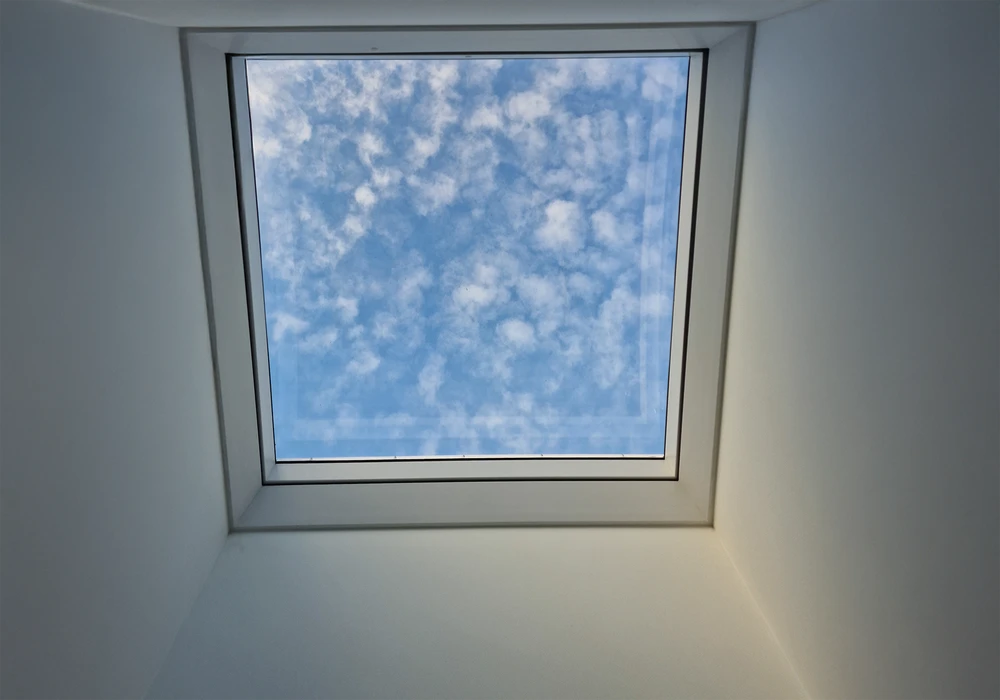 Intérieur résidentiel avec vue depuis une fenêtre de toit Velux ouverte sur toiture en tuiles terre cuite