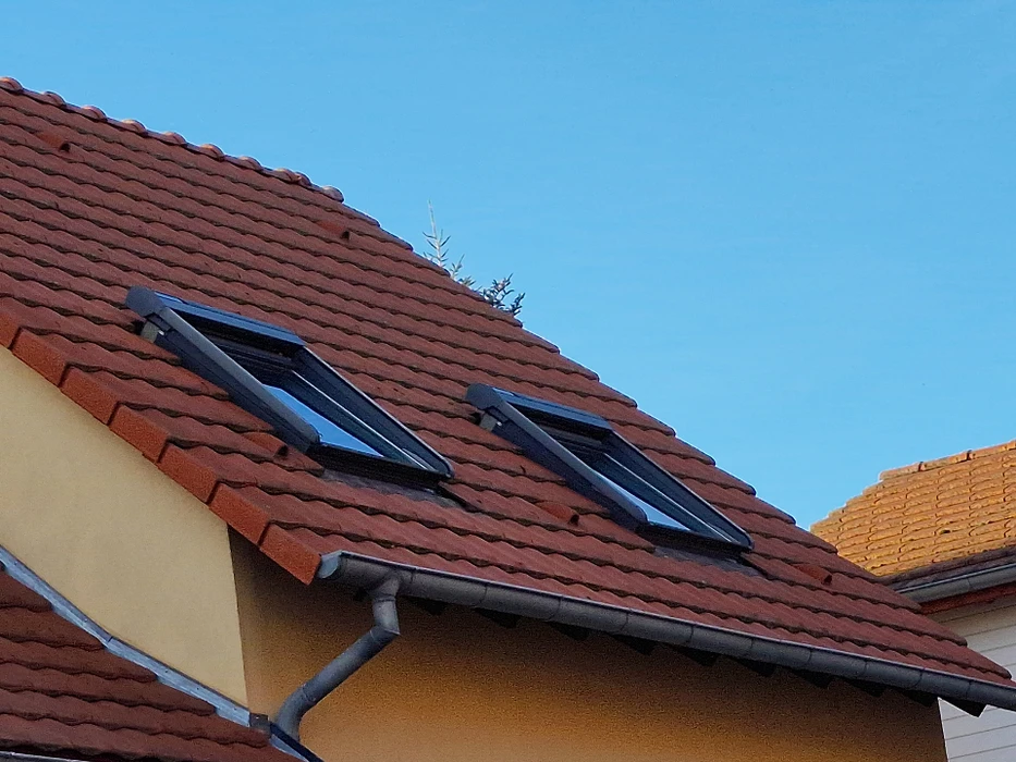 Vue intérieure d'une fenêtre de toit ouverte révélant une toiture en tuiles terre cuite