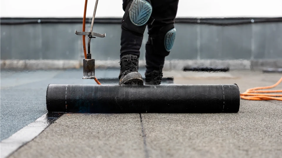 Chantier extérieur avec ouvrier en combinaison bleue installant une membrane d'étanchéité